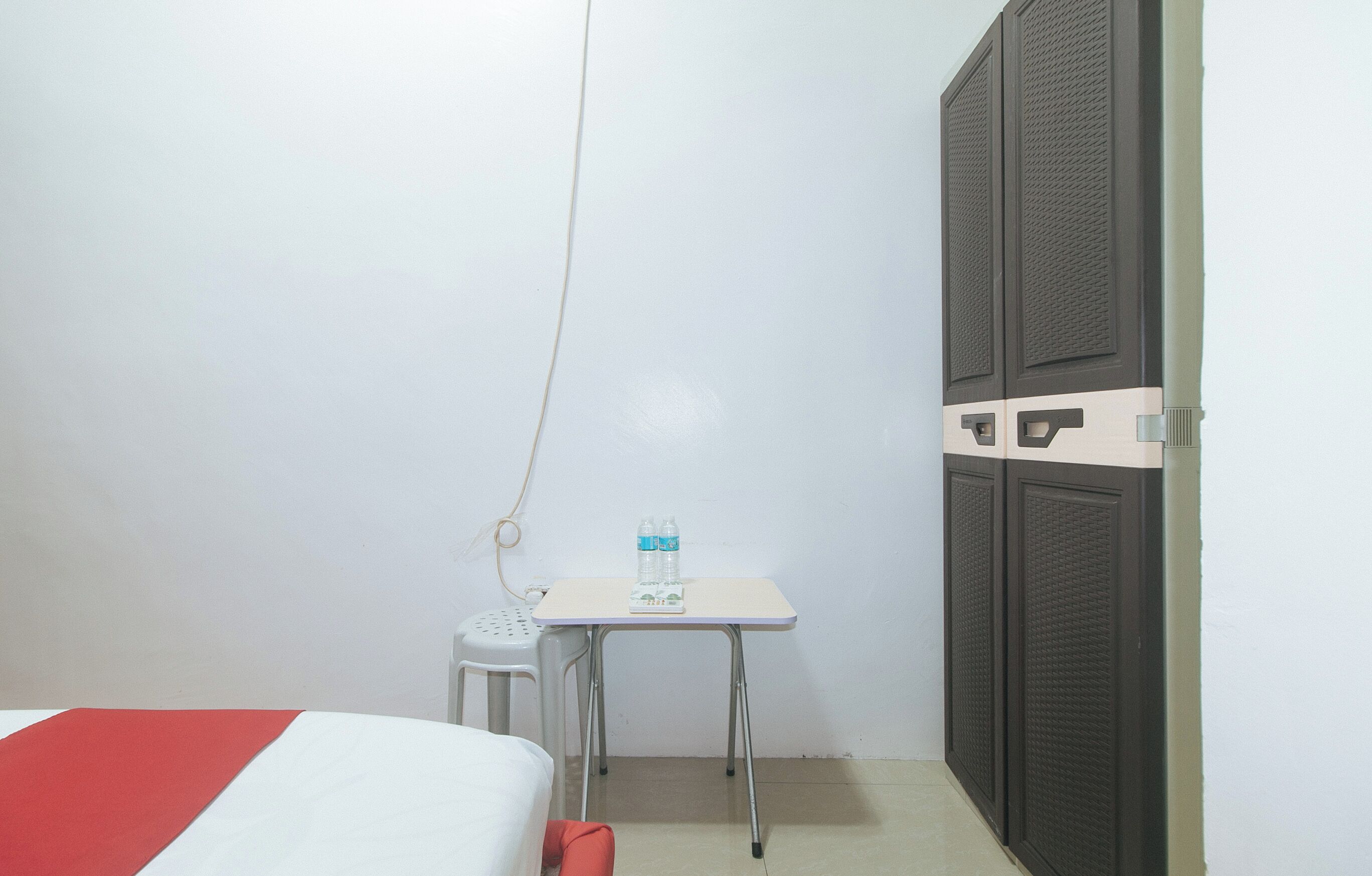 A small room with a bed, a desk with two water bottles, and a chair.