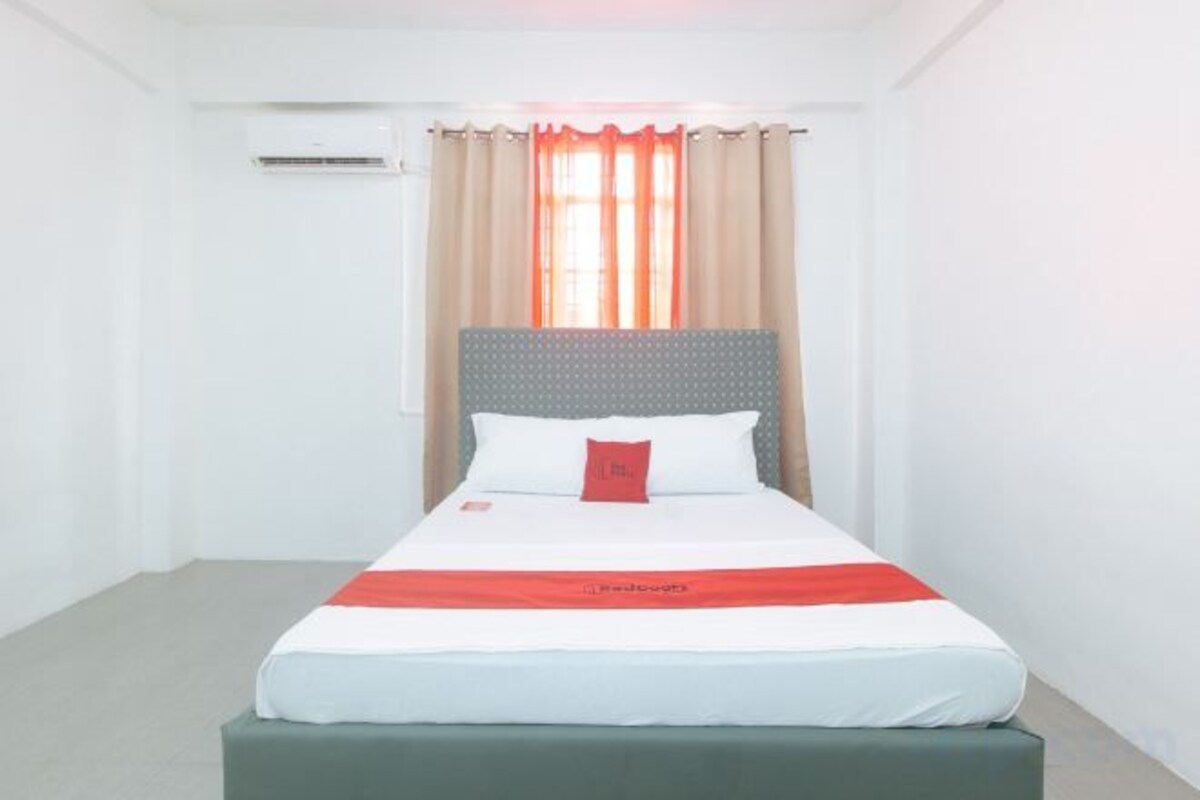 A hotel room with a bed, a headboard, and a window with curtains.