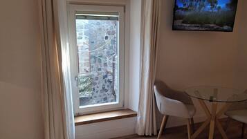Une chambre d’hôtel avec une grande fenêtre, un lit avec des serviettes soigneusement pliées, une table en verre avec des chaises et un téléviseur fixé au mur.