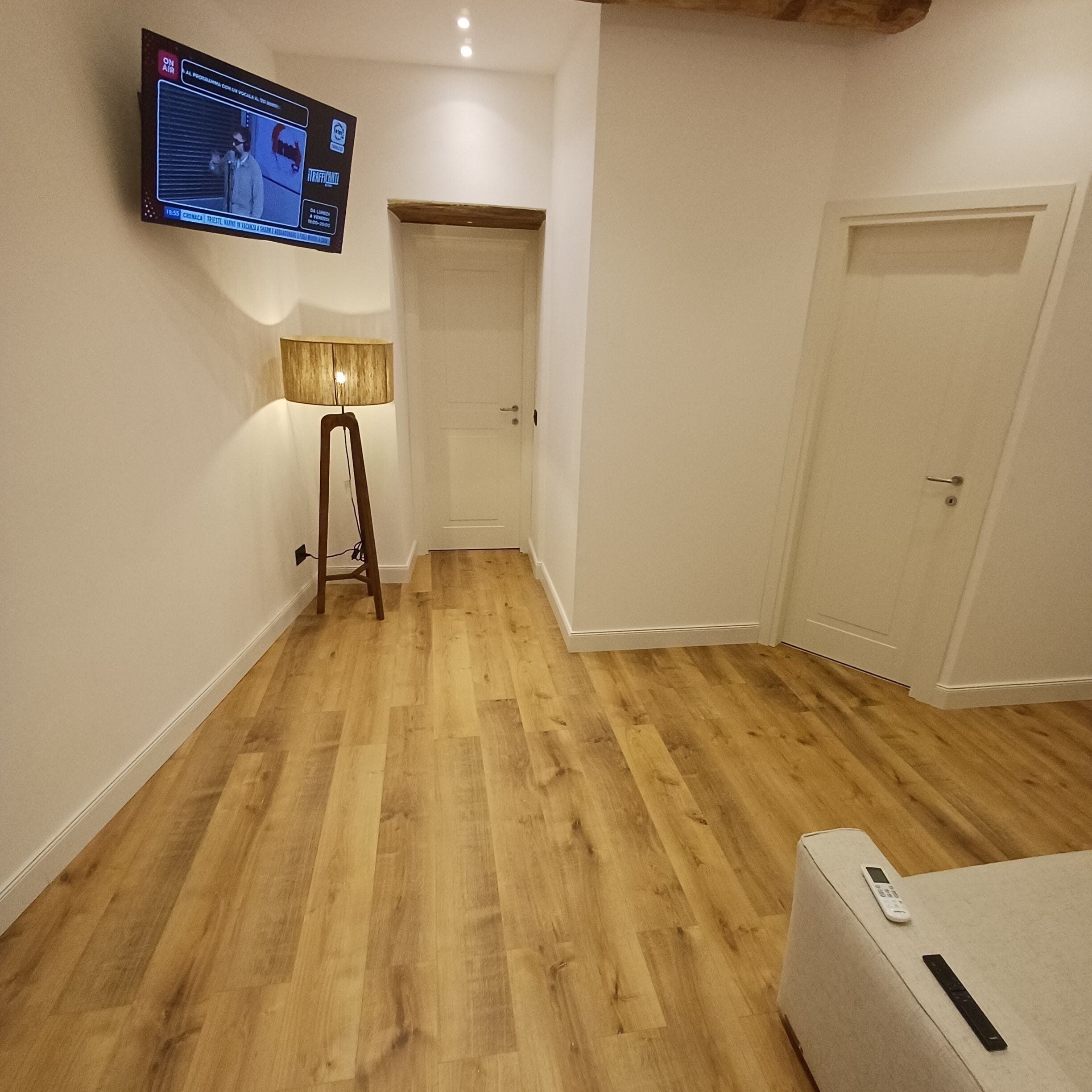 Ein Zimmer mit Holzboden, einer Stehlampe, einem an der Wand montierten Fernseher und einer Tür.