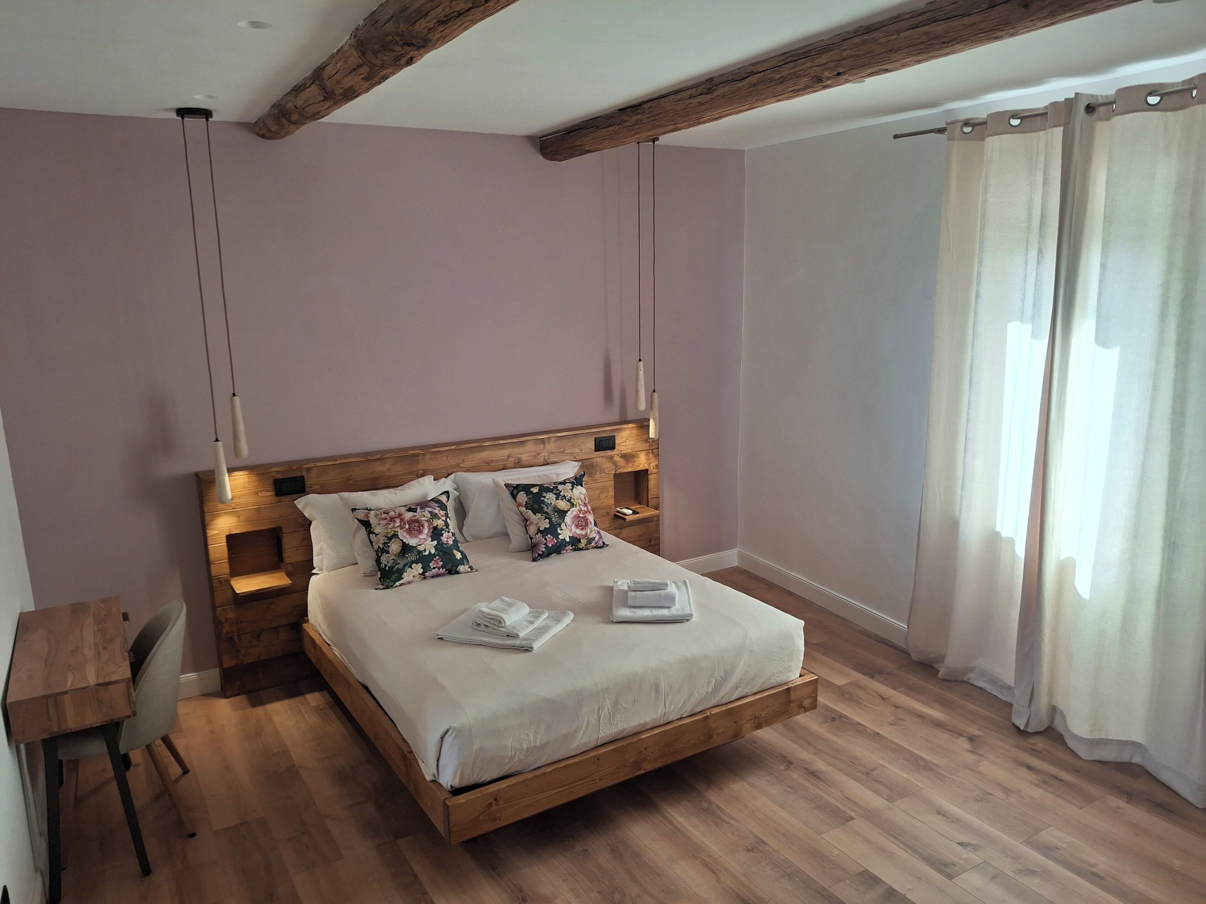A bedroom with a wooden bed, a desk, and a window with curtains.