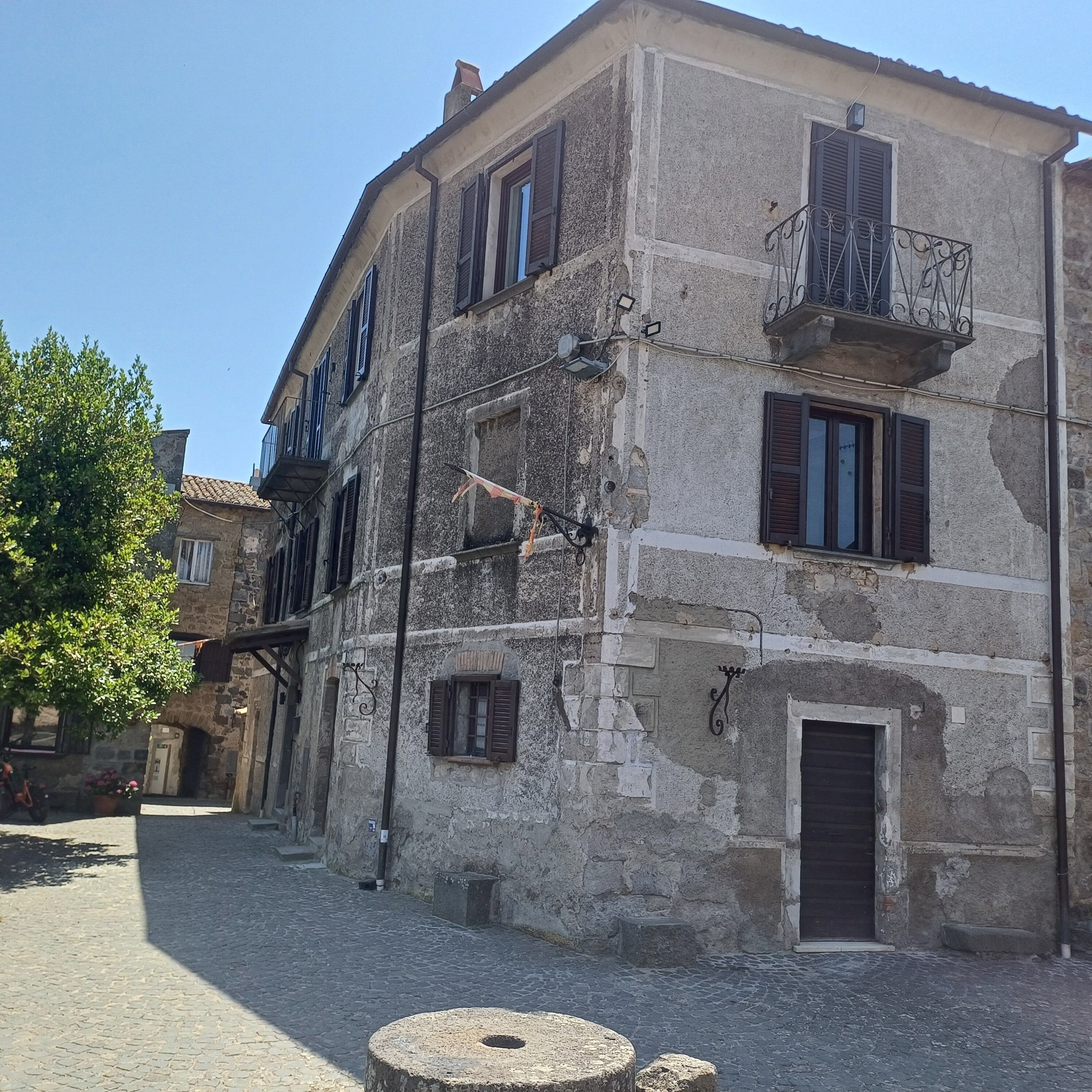 A historic stone building with multiple windows, a balcony, and a cobblestone street.