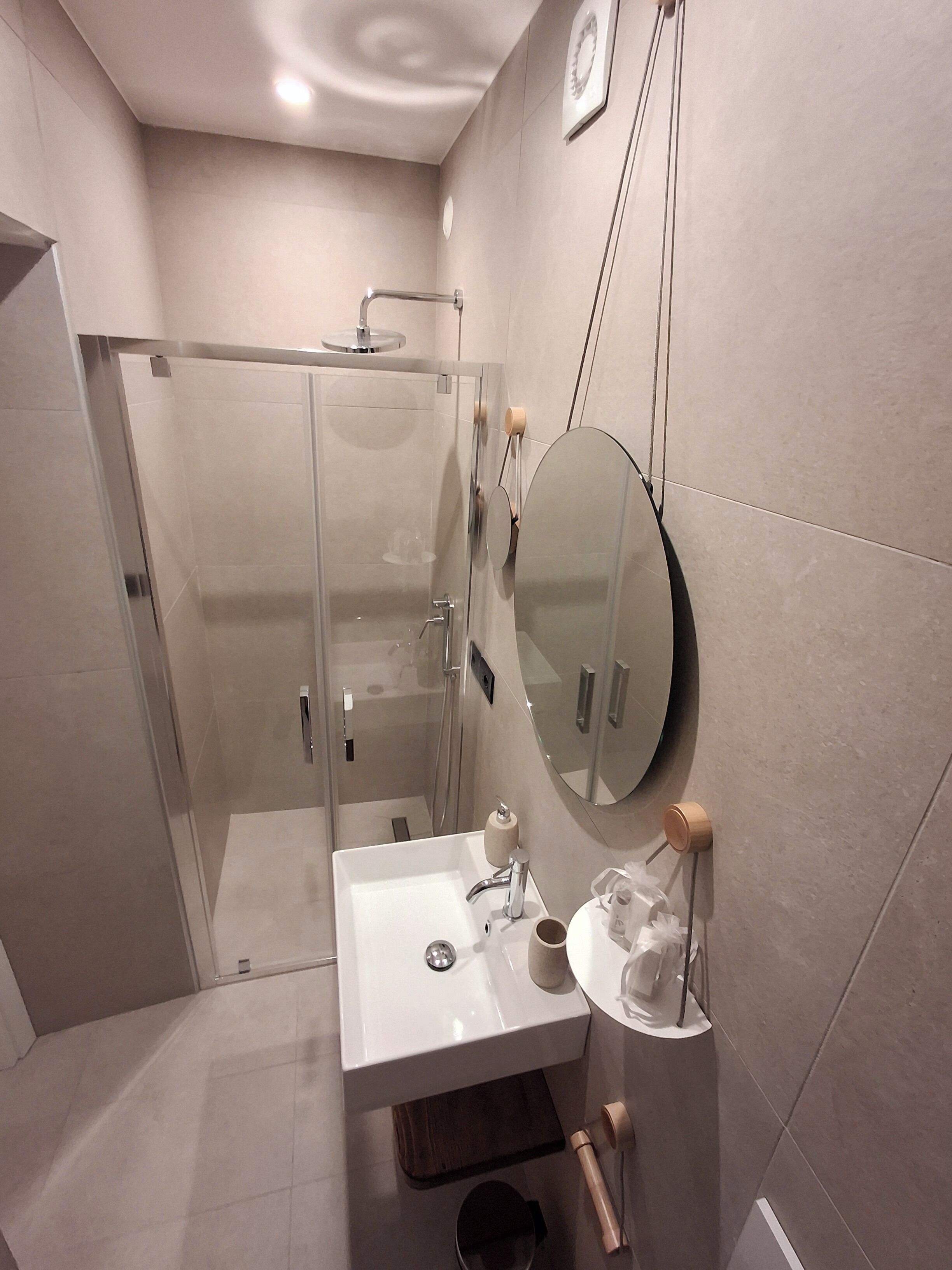 Uma casa de banho moderna com chuveiro envidraçado, lavatório branco com espelho e um porta-toalhas de madeira.