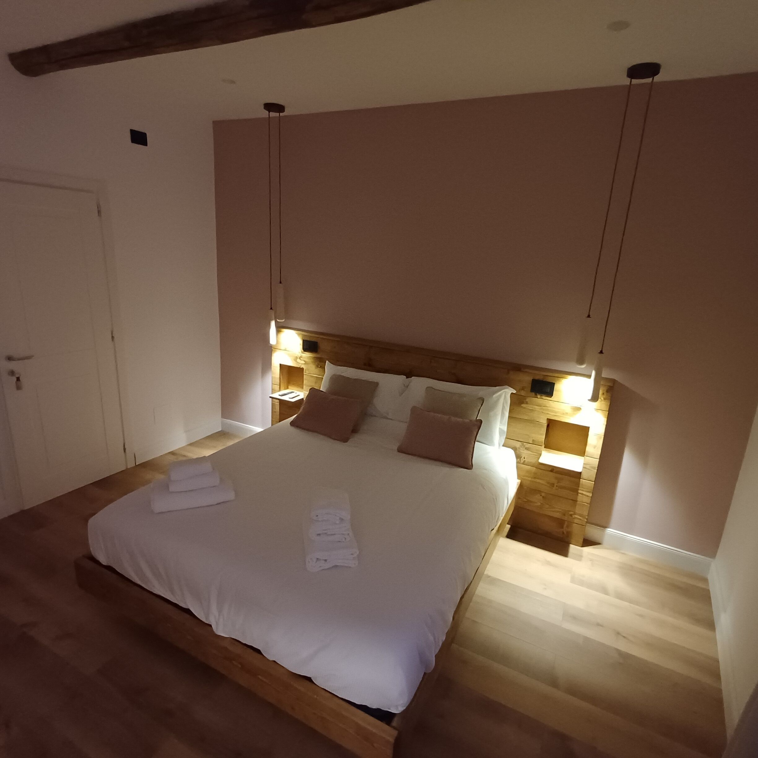 Un letto rifatto con lenzuola bianche e asciugamani piegati, una testiera in legno e lampade da comodino.
