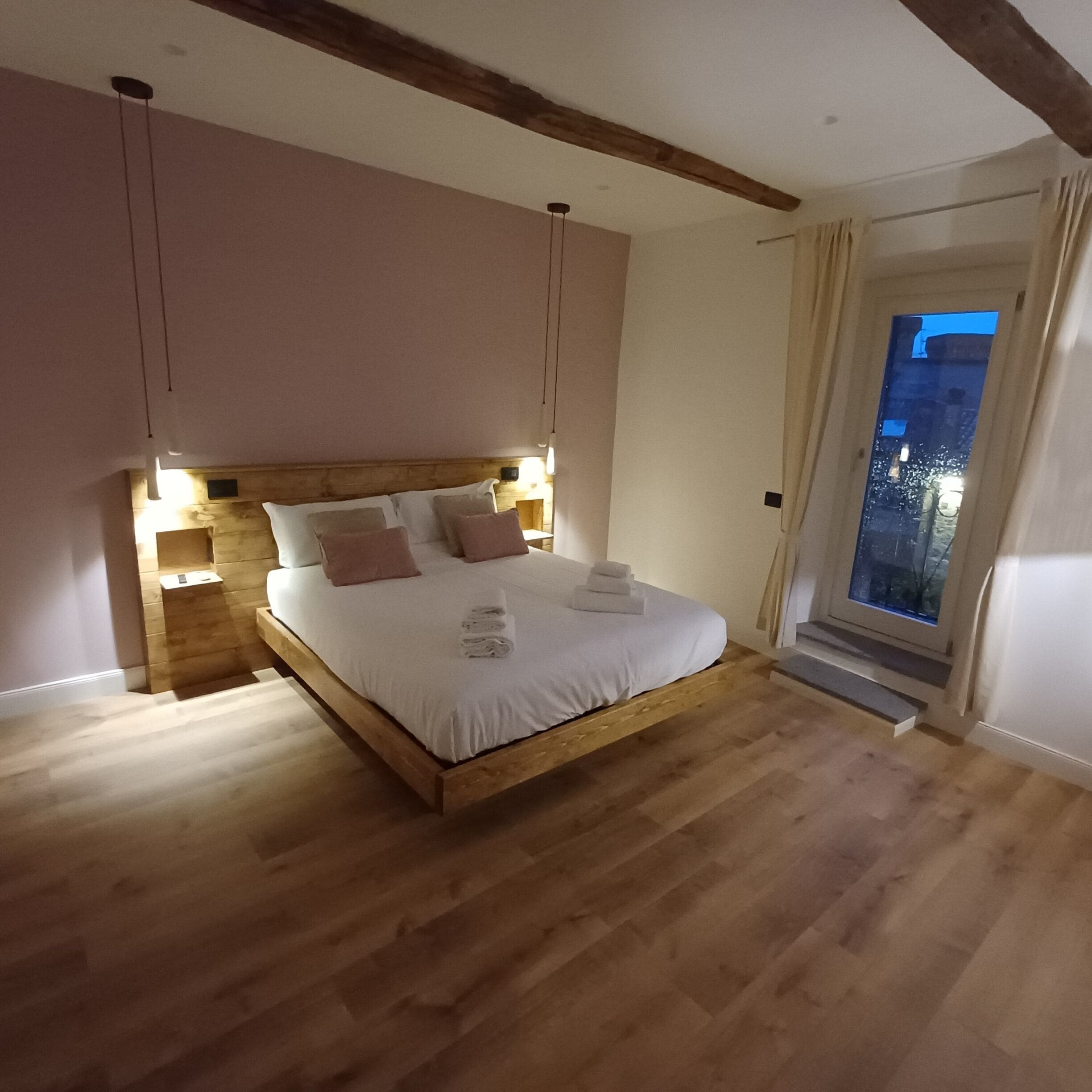 A bedroom with a wooden bed, bedside lamps, and a view of the outside.
