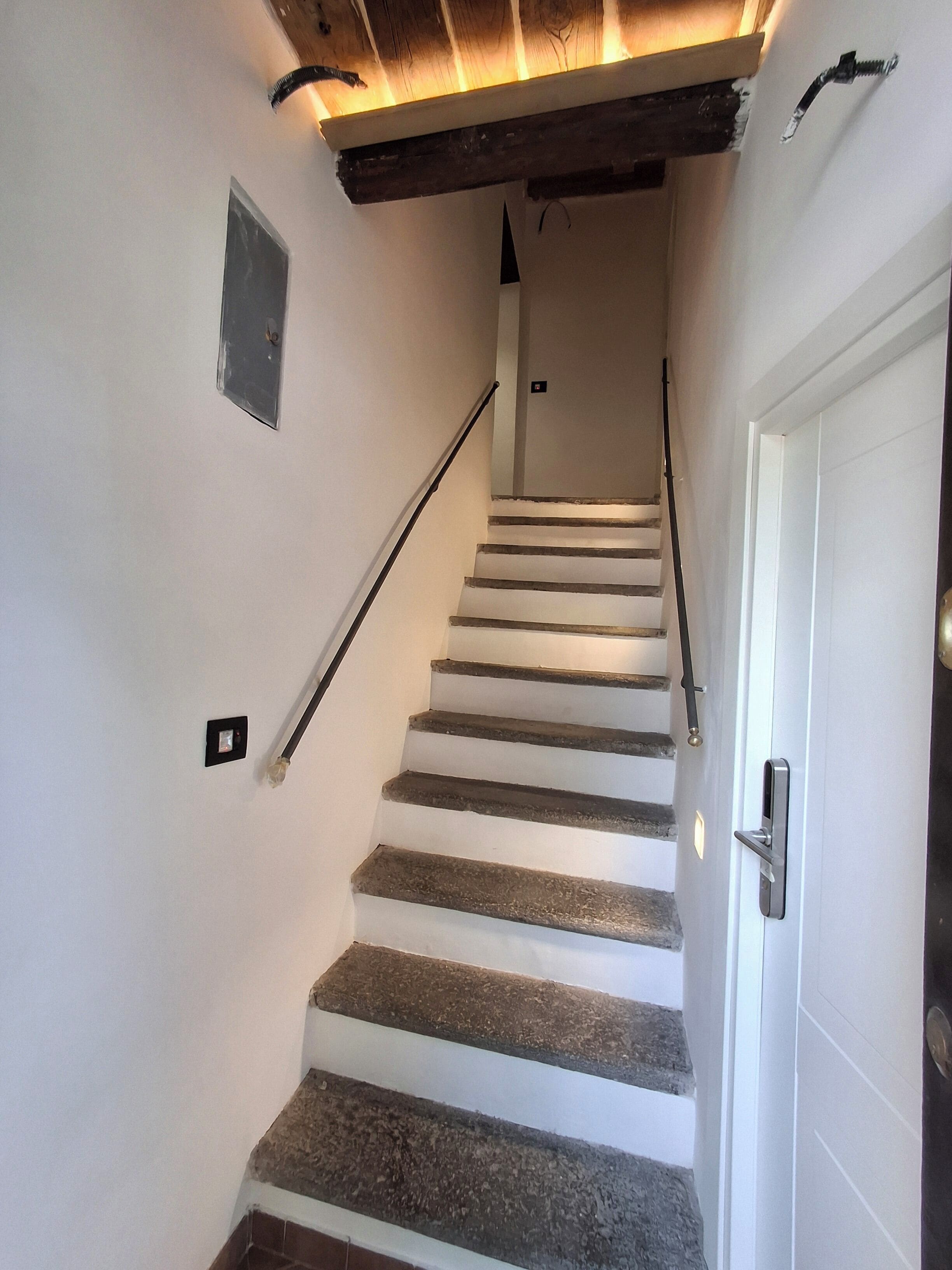 Eine Treppe mit weißen Wänden und steinernen Stufen, die zu einer Tür führt.