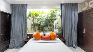 A modern bedroom with a large bed, grey curtains, wooden wardrobe, and a view of greenery through the window. - Villa Naema - 4 BR Private Villa (Seminyak)