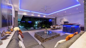 A modern living room with a large sofa, a coffee table, and a bar area with stools. - Villa Naema - 4 BR Private Villa (Seminyak)