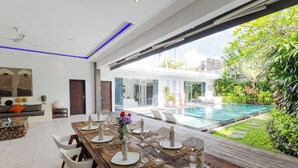 A dining area with a wooden table set for six, overlooking a swimming pool and lush greenery. - Villa Naema - 4 BR Private Villa (Seminyak)