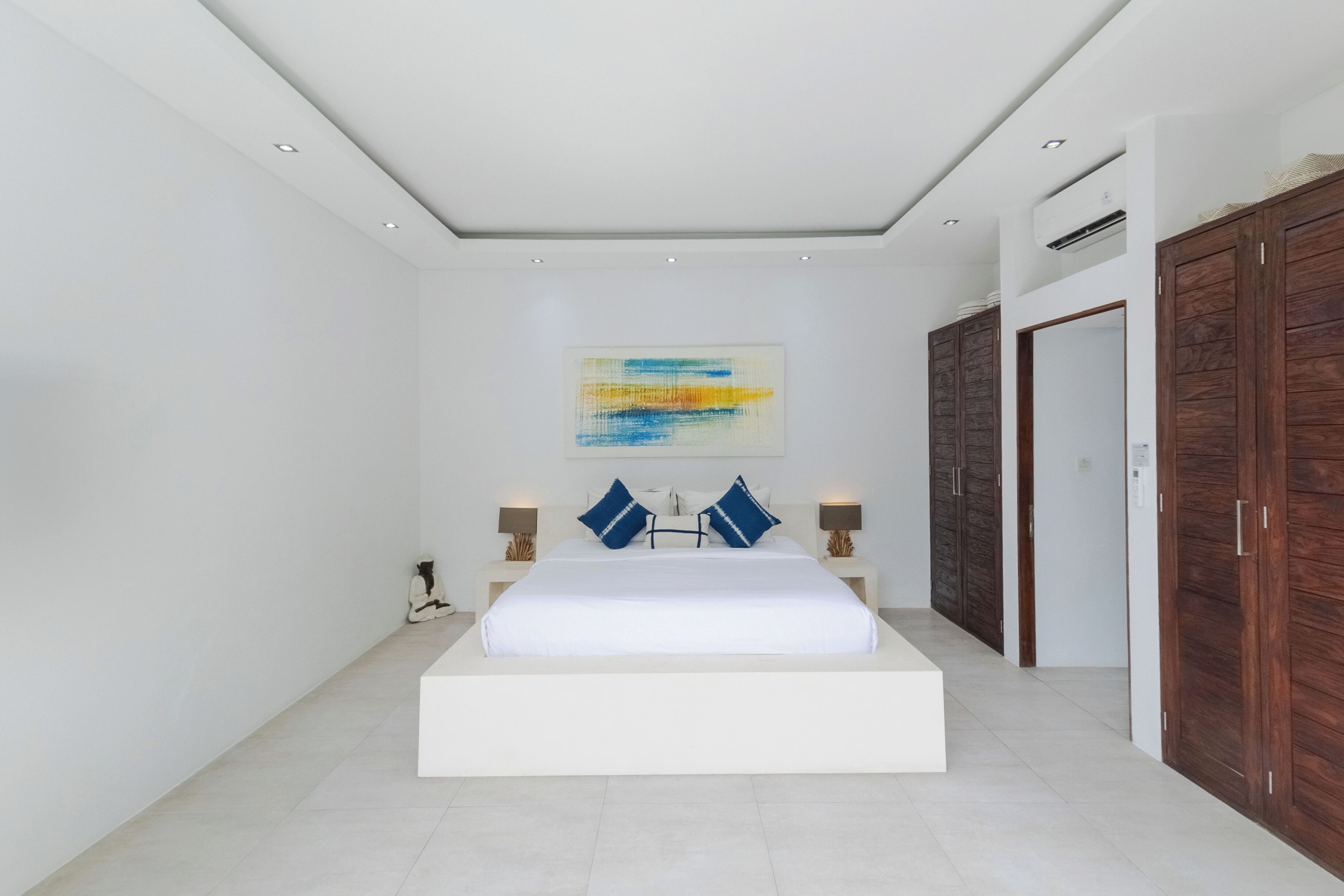 A modern bedroom with a large bed, a ceiling light, and a wall-mounted air conditioner.