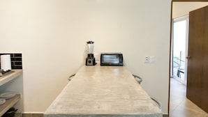 Une cuisine équipée d’un plan de travail, d’un mixeur, d’un grille-pain et d’une porte donnant sur un espace extérieur.