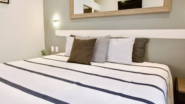 Une chambre d’hôtel avec un grand lit, une tête de lit, un miroir et une petite plante.
