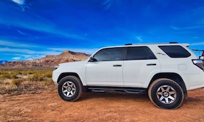 A white SUV parked in a desert landscape with a mountain in the background.