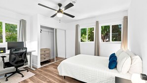 A bedroom with a bed, a desk with a computer, a chair, a wardrobe, and a ceiling fan.