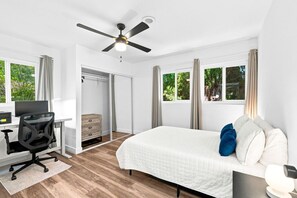 A bedroom with a bed, a desk with a computer, a chair, a wardrobe, and a ceiling fan.