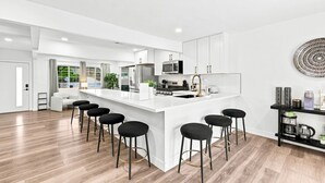 A modern kitchen with a central island, bar stools, and a view of the outdoors.