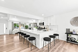 A modern kitchen with a central island, bar stools, and a view of the outdoors.