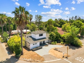 A two-story house with a patio, surrounded by palm trees and other greenery.