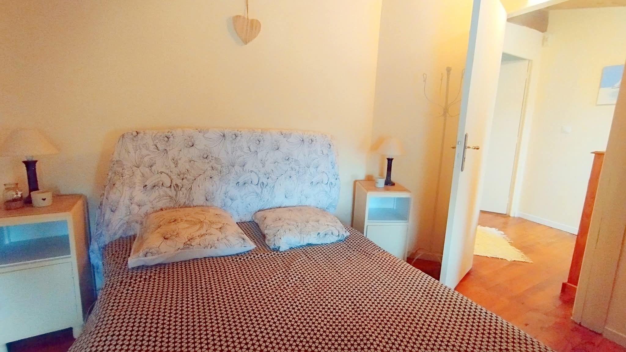 A bedroom with a patterned bedspread, two pillows, a heart-shaped wall decoration, and bedside lamps.