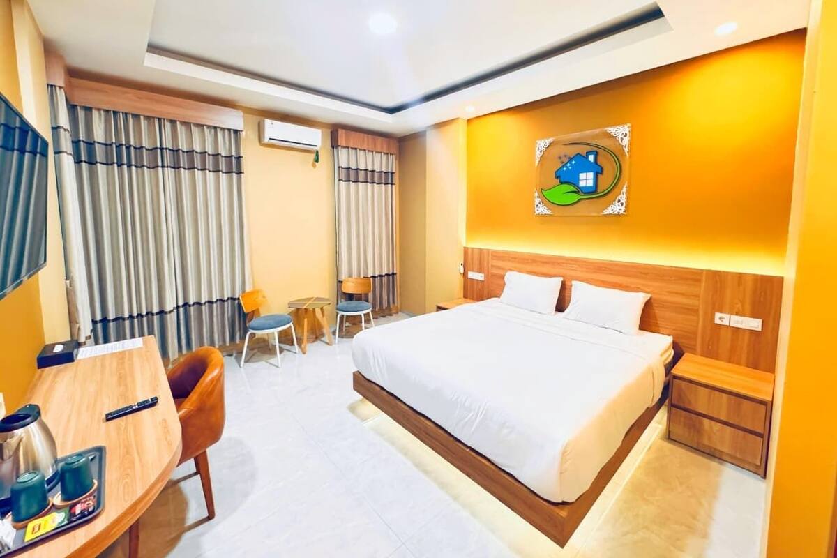 A hotel room with a large bed, a desk with a chair, a small table, and a wall-mounted TV.