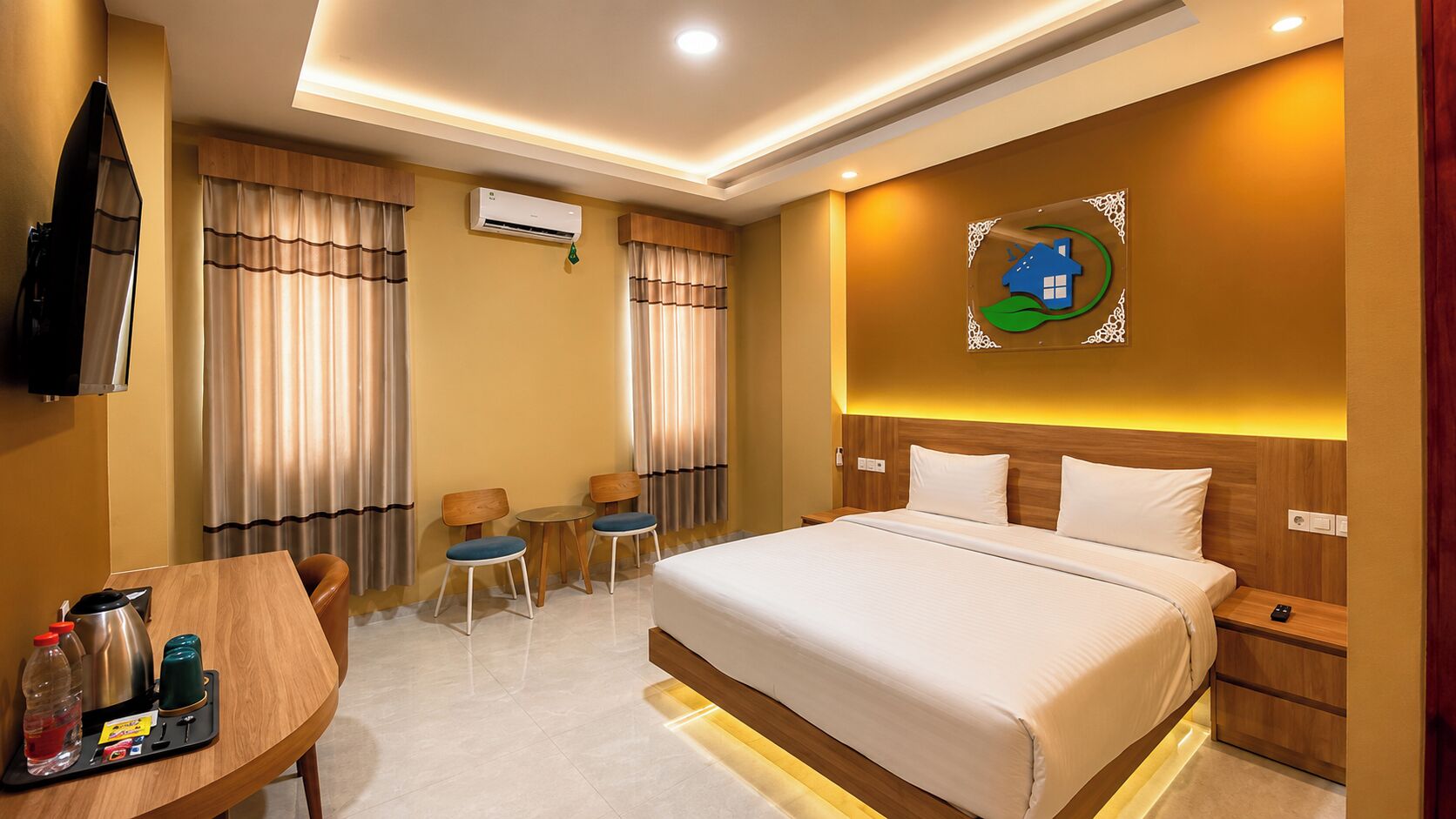 A hotel room with a bed, a desk with chairs, an air conditioning unit, and a wall-mounted artwork.