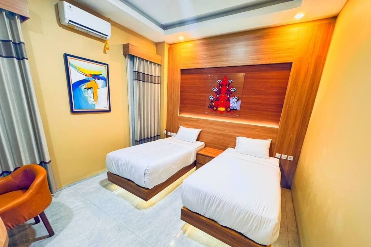 A hotel room with two beds, a wooden headboard, a framed artwork, and a single orange chair.