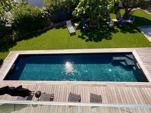 Piscina retangular com deck de madeira, rodeada por um gramado bem cuidado e árvores.