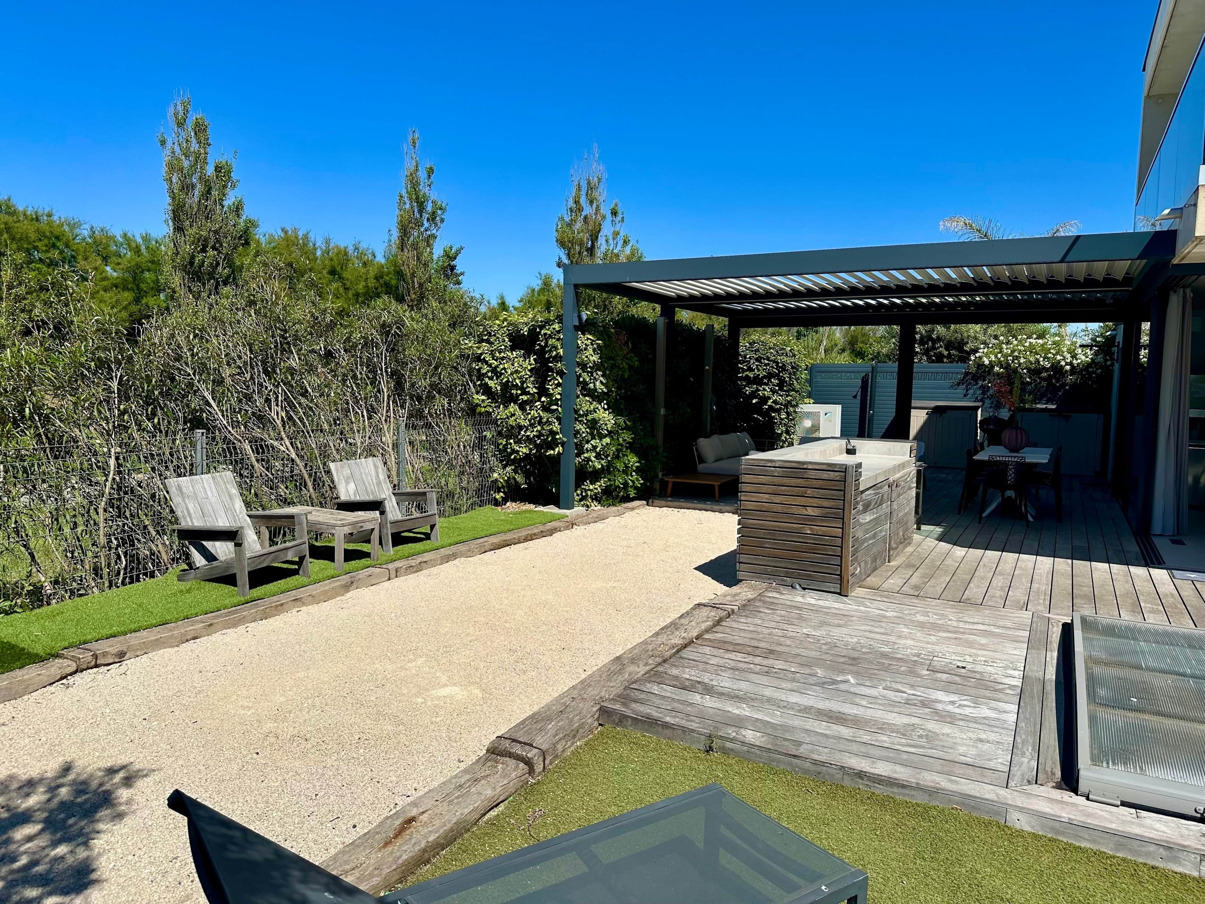 Ein überdachter Patio-Bereich mit Gartenmöbeln, einem Grill und einem kleinen Tisch.