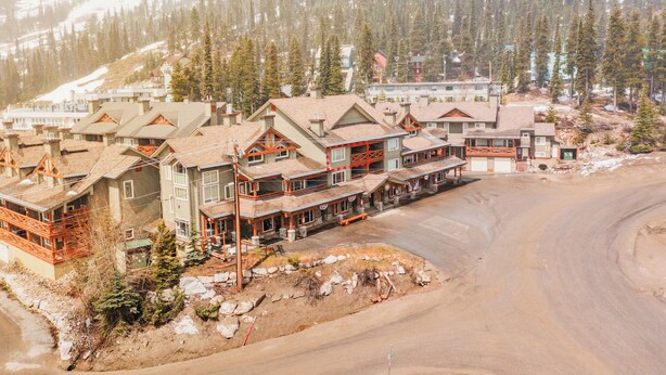 A resort with multiple buildings, a dirt road, and a forested mountain backdrop.