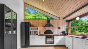 A modern kitchen with wooden cabinets, a black refrigerator, and a large window offering a view of greenery. - "Rosaline" - 500m from the sea by Interhome (Grenaa)