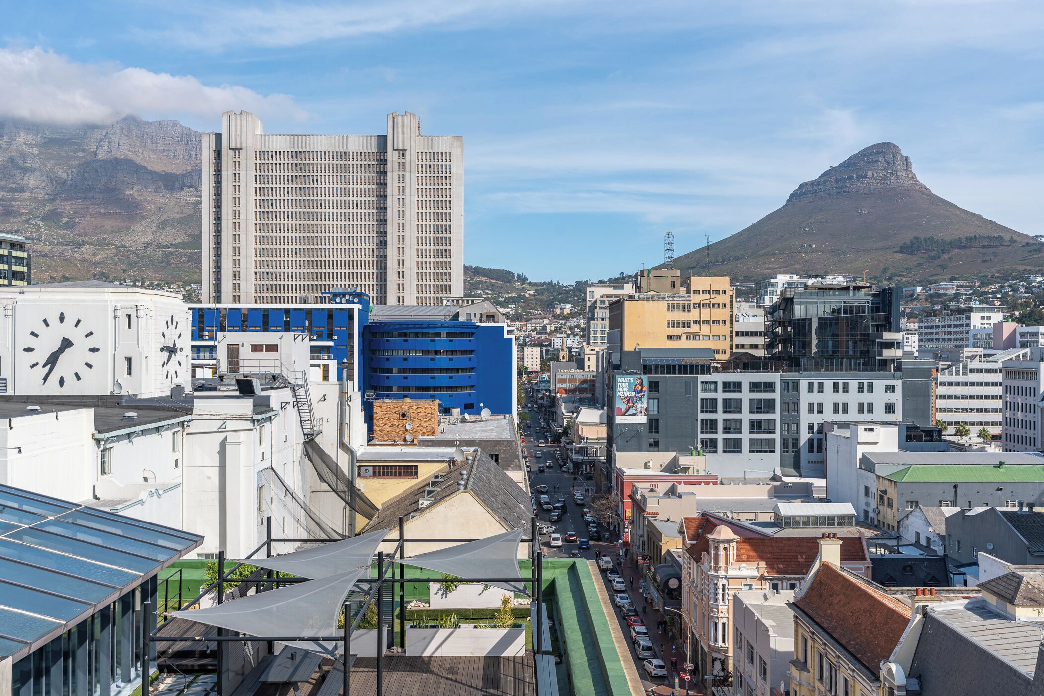 A cityscape with a prominent clock tower, modern buildings, and a mountain in the background.