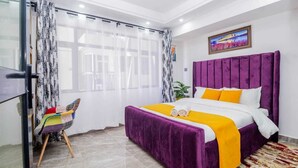 Un dormitorio moderno con una cama grande, ropa de cama morada y una silla colorida.