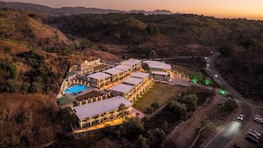 A large, multi-story hotel with a swimming pool, surrounded by hilly terrain and a winding road. - Jaldhara Resort (Kumbhalgarh)