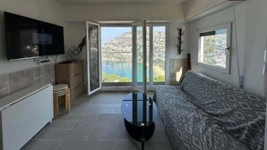 Un espacio habitable pequeño con kitchenette, sofá, televisor y balcón con vistas panorámicas.
