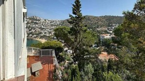 Un balcón con vistas a un pueblo costero, una montaña al fondo y un alto pino en primer plano.
