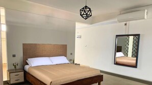 A modern bedroom with a wooden bed, a nightstand, a bedside table, a hanging light fixture, and a wall-mounted air conditioning unit. - THE LIGHT VILLA (Trou d'Eau Douce)