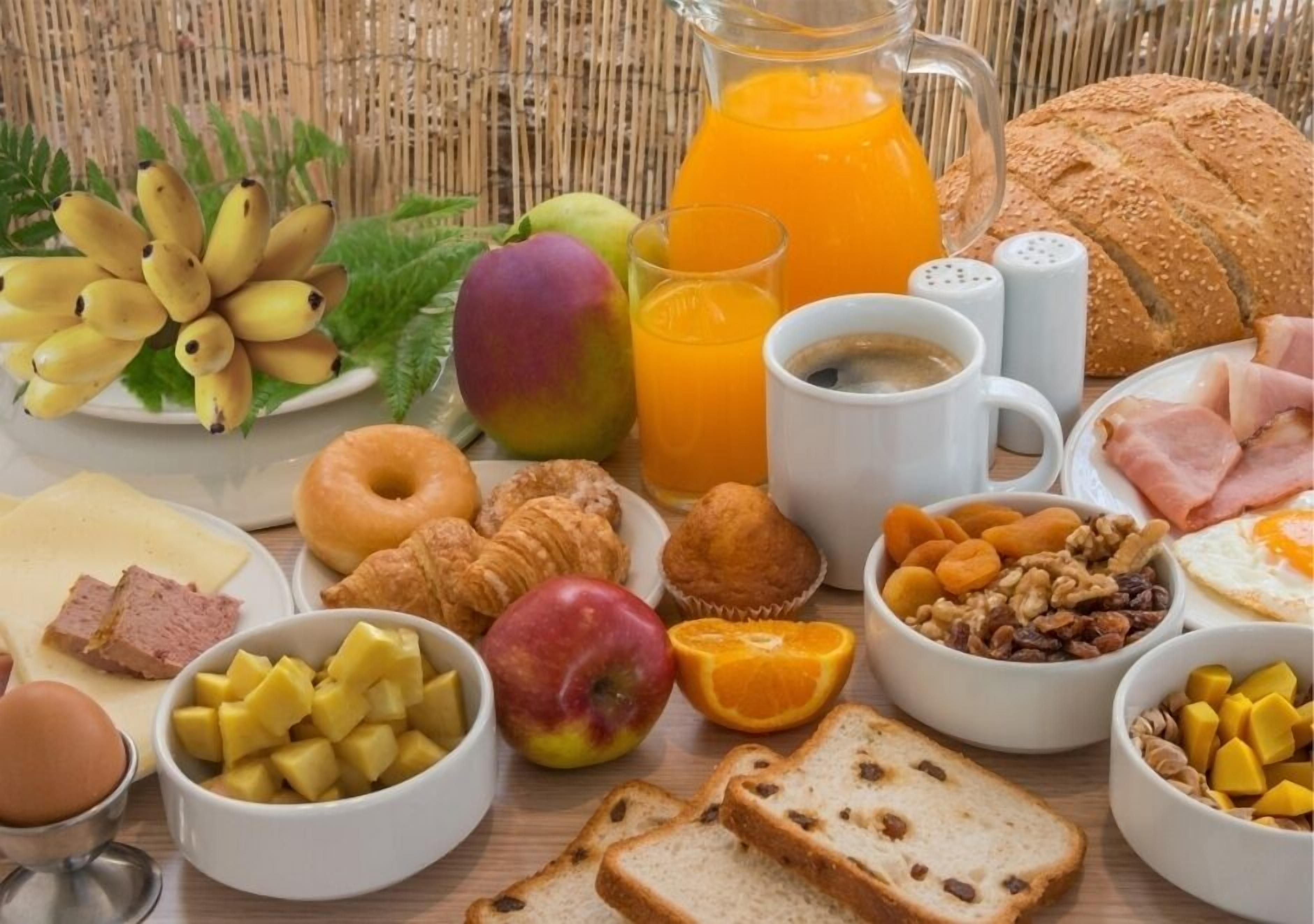 A breakfast table with various food items including bread, fruits, pastries, and beverages.