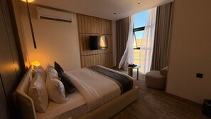 A modern hotel room with a large bed, a flat-screen TV, a small table, and a view of the outdoors. - White Season Hotel (Haql)