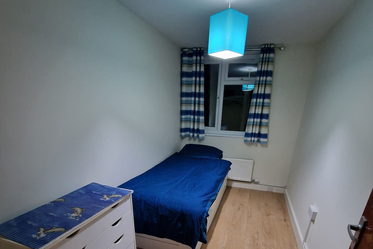 Un dormitorio con cama, cómoda, ventana con cortinas y una lámpara en el techo.