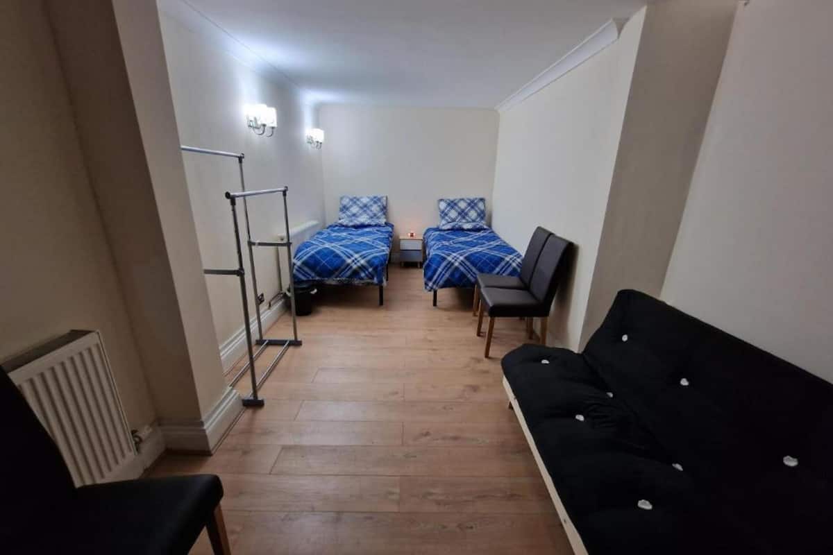 Una habitación pequeña y funcional con dos camas, un sofá negro y un radiador.