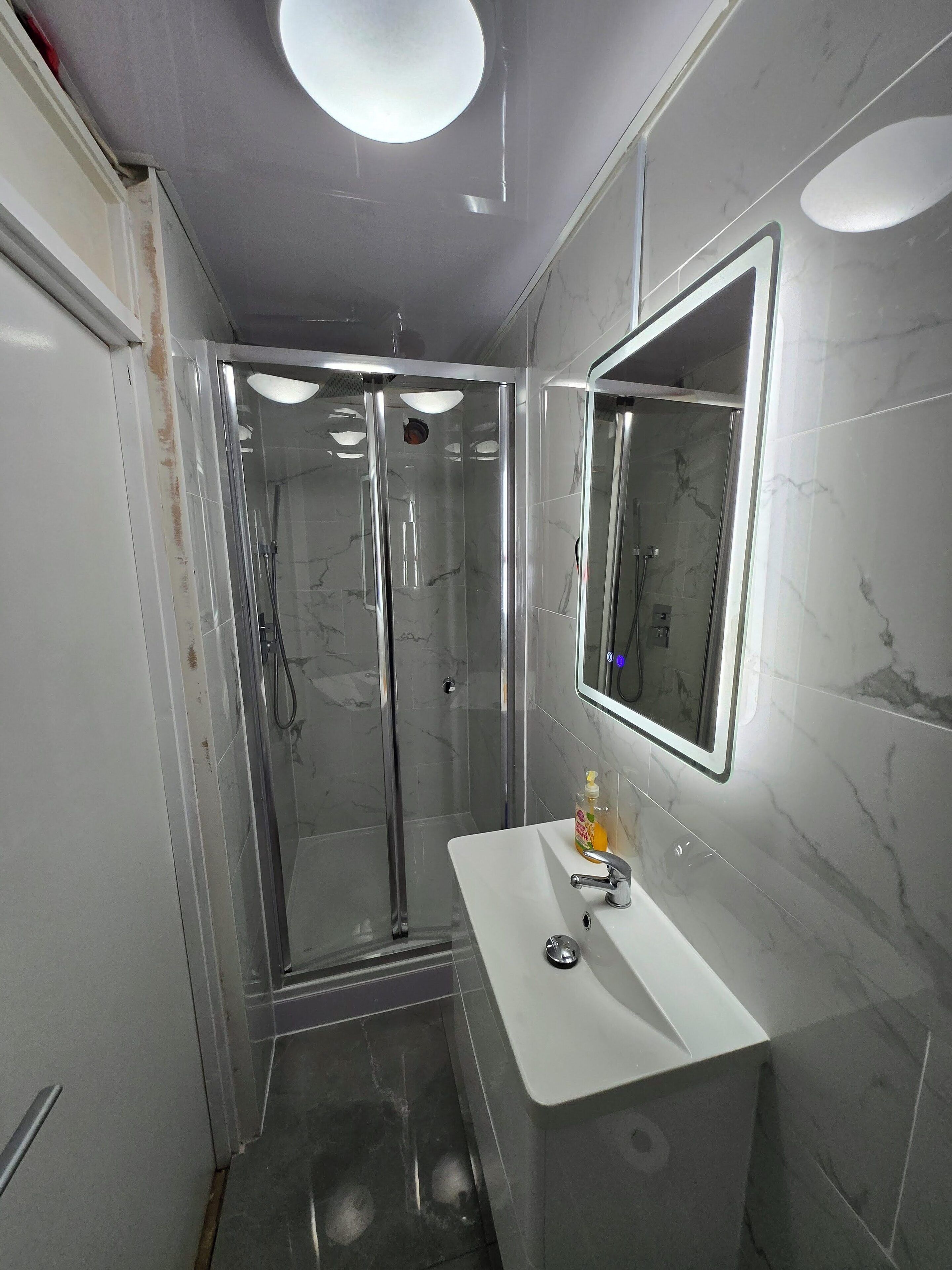 A modern bathroom with a glass-enclosed shower, a white sink with a mirror, and marble-patterned walls.