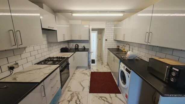 Een moderne keuken met witte kasten, een gasfornuis, een wasmachine en een magnetron.