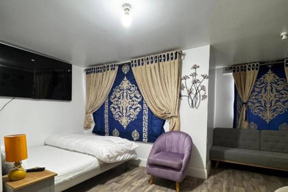 A bedroom with a bed, a chair, a sofa, and a lamp.