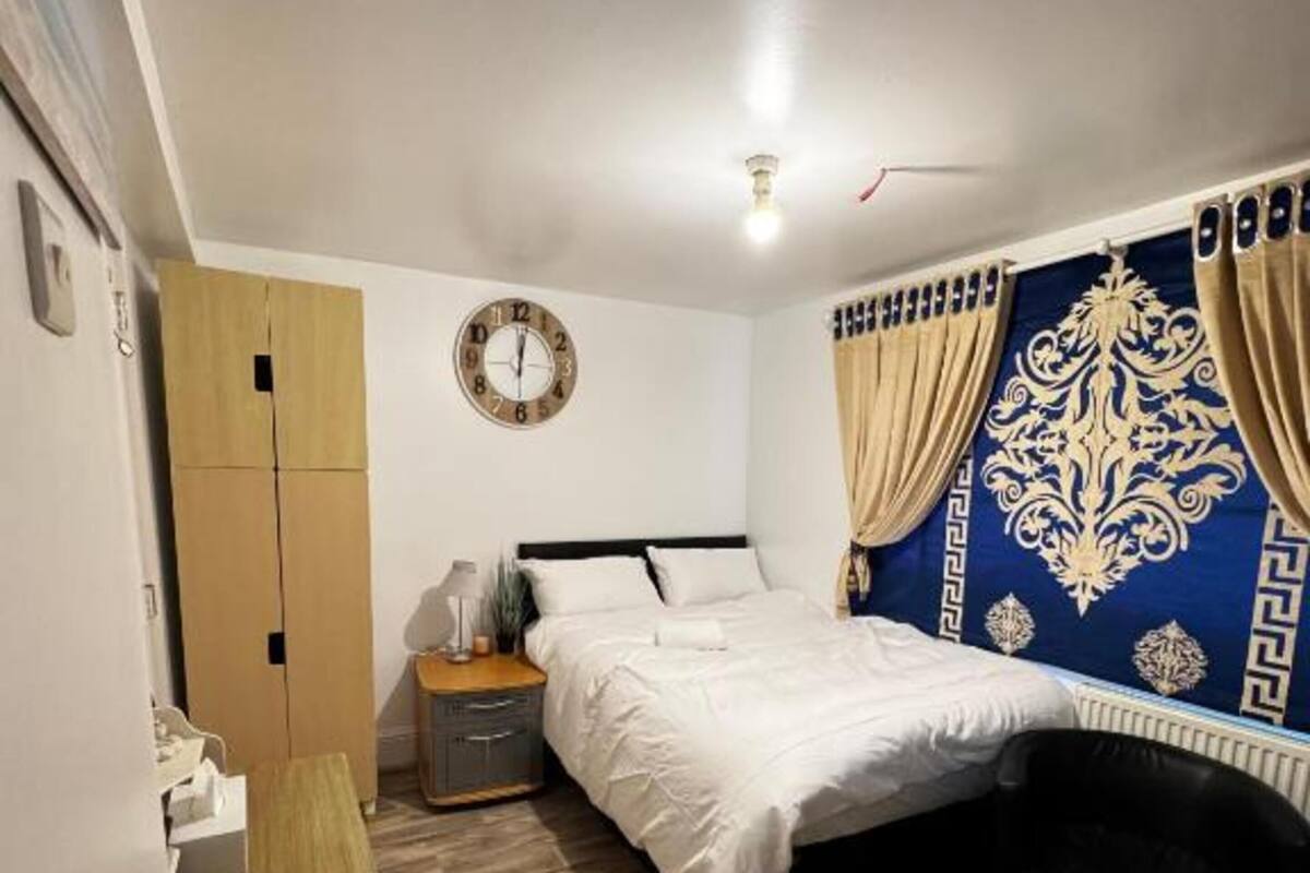 A bedroom with a bed, bedside table, lamp, and a wall clock.