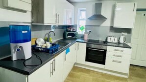 A compact kitchen with white cabinets, a black countertop, and a water dispenser.