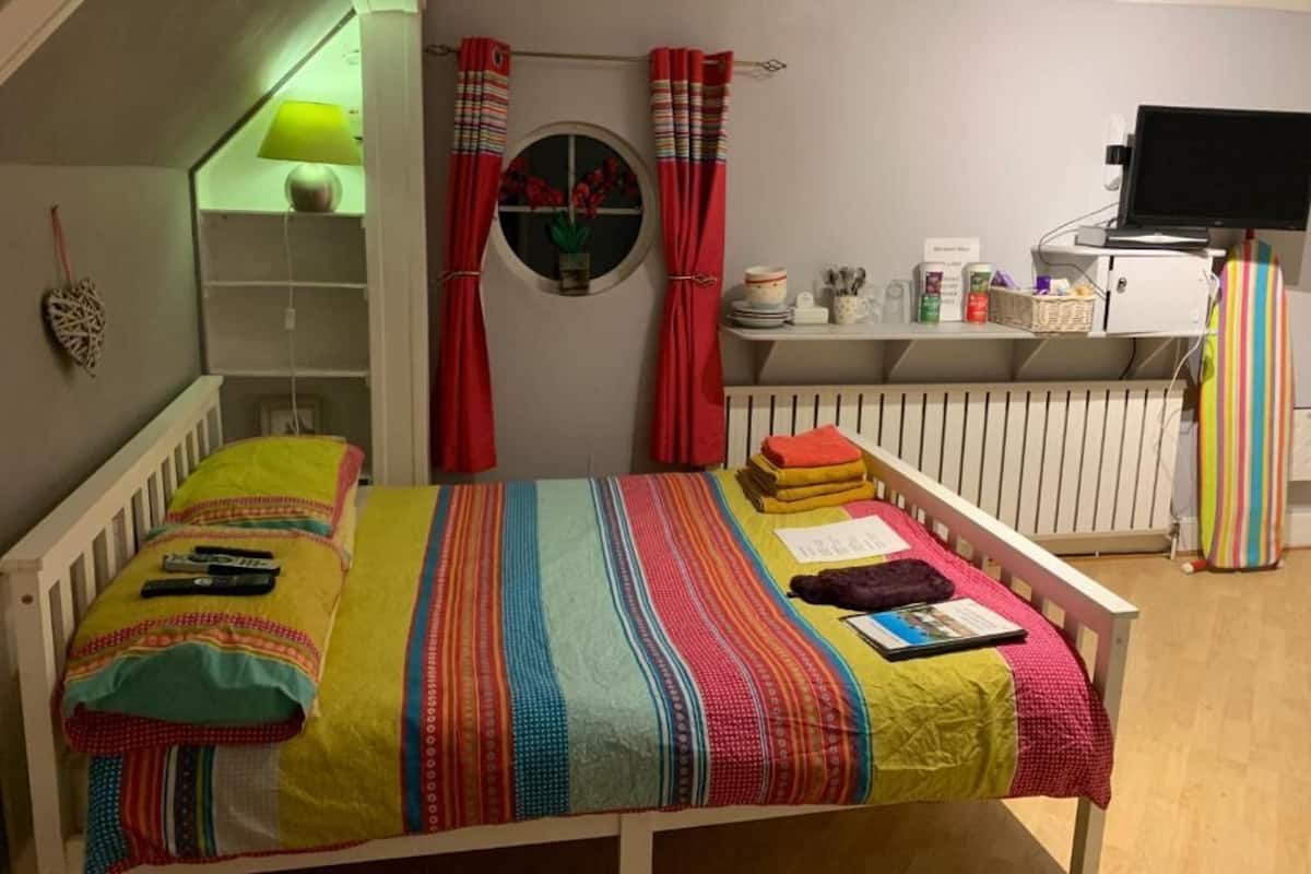 Ein gemütliches Schlafzimmer mit einem Bett, einem Regal mit verschiedenen Gegenständen, einem Fenster mit Vorhängen und einem Fernseher.