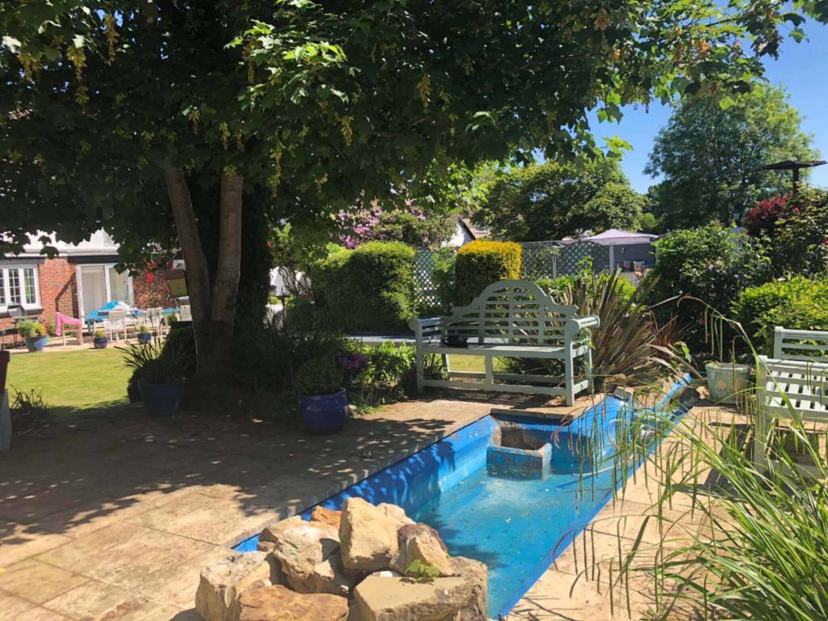 Une piscine bordée de pierres, entourée de plantes en pot et agrémentée d’un banc en bois.