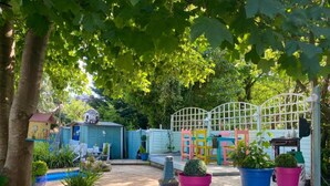 Ein Garten mit einer Holzterrasse, Blumentöpfen, einem Vogelhäuschen und einem kleinen Schuppen.