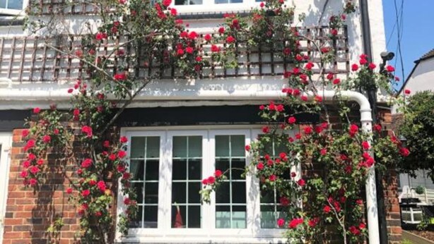 Ein zweistöckiges Haus mit Ziegelverkleidung, weißen Fenstern und einem Balkon mit roten Blumen.