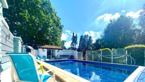 Ein Schwimmbecken mit gefliestem Beckenrand, umgeben von Bäumen und einem Zaun.